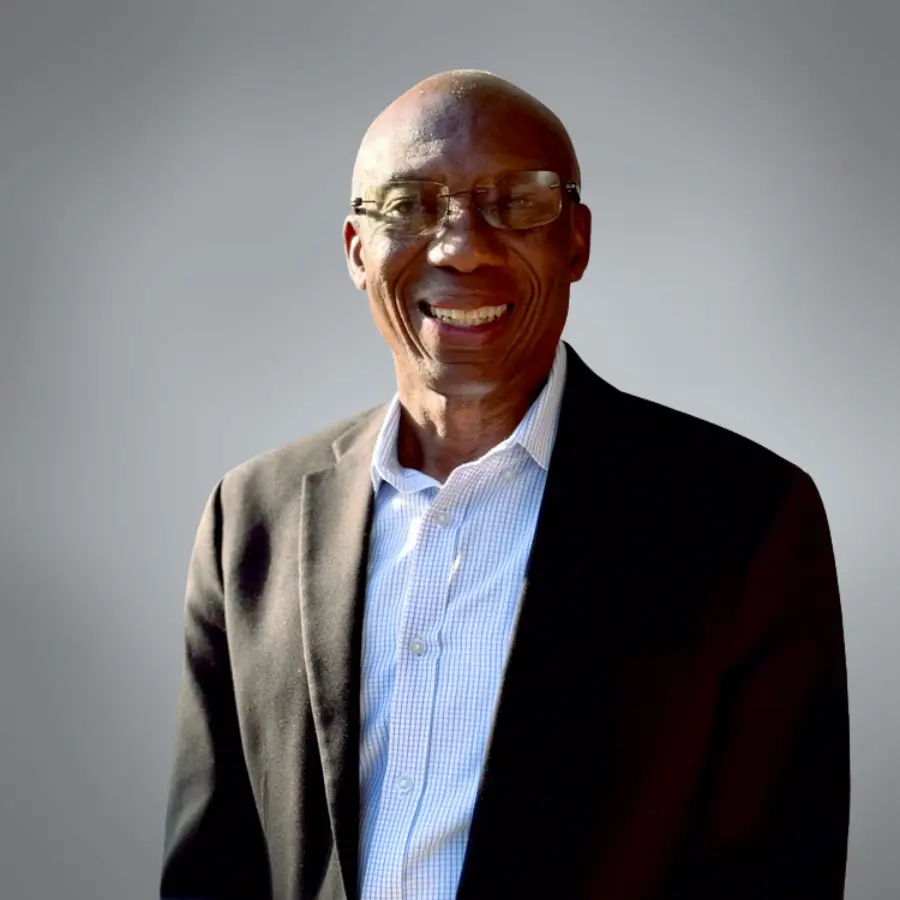 Smiling man in a dark blazer and light blue checkered shirt posing for a professional portrait.