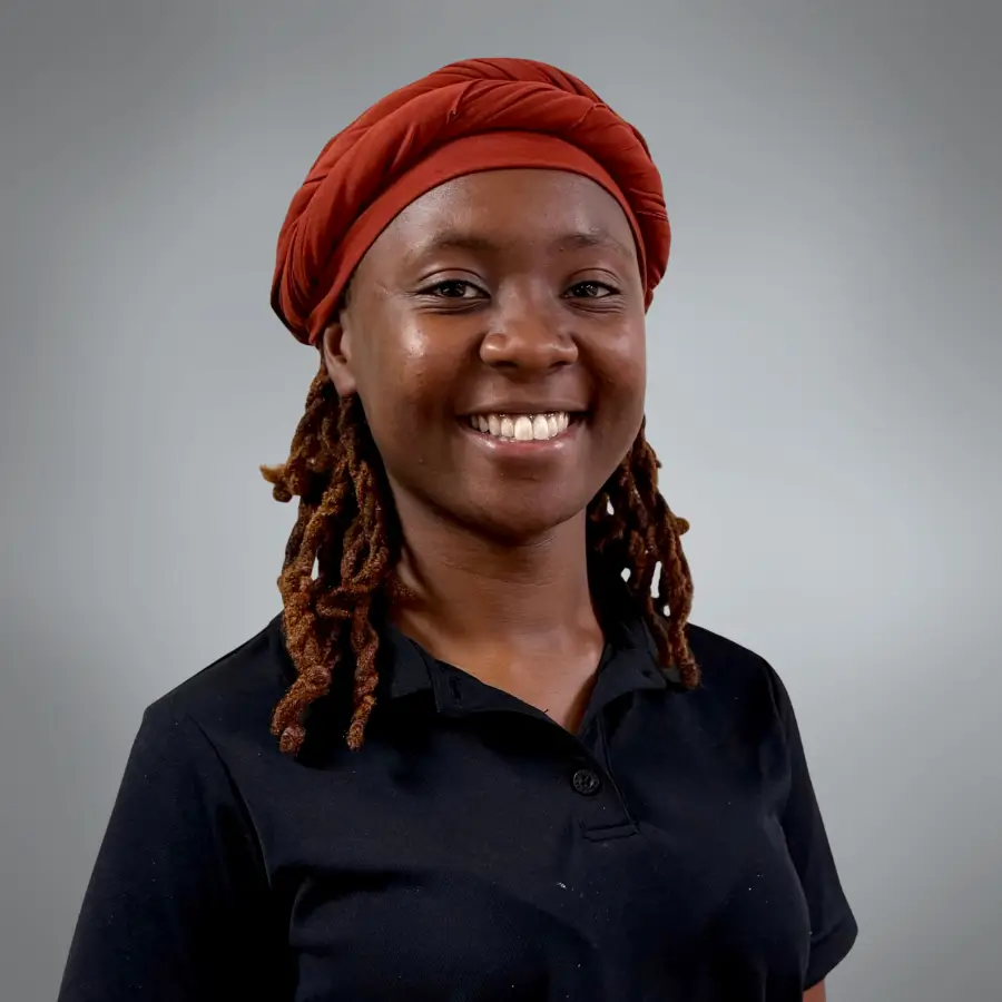 Portrait of a smiling woman wearing a red headwrap and black polo shirt against a gray studio backdrop.